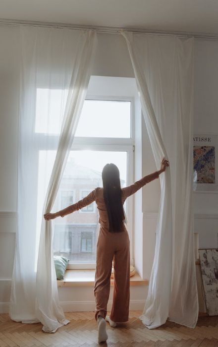 a girl is opening the drapes, showing how long should drapes be